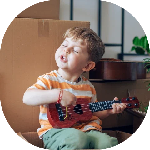 Child playing ukulele in cardboard box